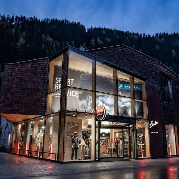 Modernes Gebäude mit großer Glasfassade, beleuchtetem Innenraum und Schaufenster mit Sportartikeln.